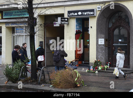 Passanten schauen Blumen und Kerzen, die um ein Foto von David Bowie vor ehemalige Residenz des Sängers an Hauptstrasse 155 in Berlin, Deutschland, 11 Januar 2016 gelegt wurde. Eine Karte, die zwischen den Blumen platziert wurde liest "Für David, Thank You for the Music!". Bowie starb am 10. Januar 2016 an Krebs. Foto: Jens Kalaene/dpa Stockfoto