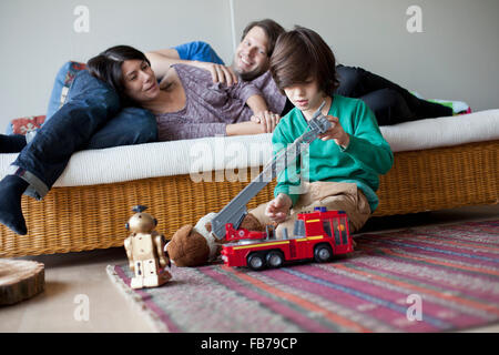Jungen spielen mit Spielzeug, Mutter und Vater auf Sofa im Hintergrund Stockfoto
