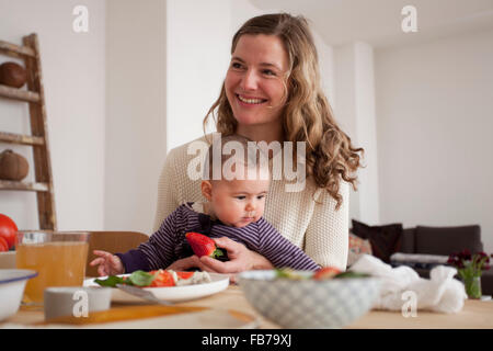 Lächelnde Frau sitzend mit Baby Girl zu Hause wegschauen Stockfoto