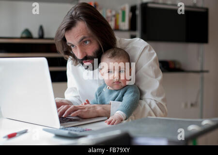 Mann, sitzend mit Baby Girl zu Hause am Laptop arbeitet Stockfoto