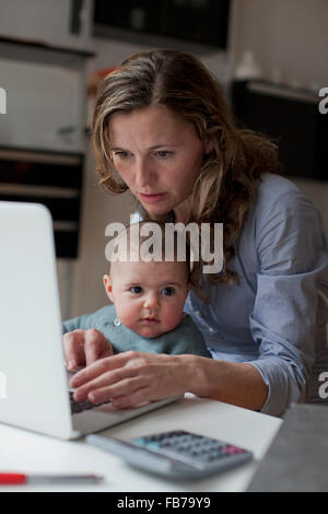 Frau auf Laptop sitzend mit Baby Girl zu Hause arbeiten Stockfoto