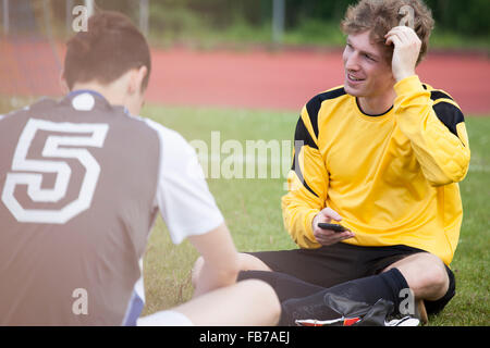 Junge Sportler sitzen mit Freund auf Fußballplatz Stockfoto