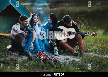 Mann, die Gitarre zu spielen, während Sie mit Freunden am Lagerfeuer sitzen Stockfoto