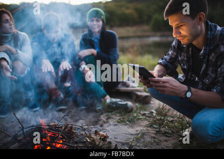 Junger Mann mit digital-Tablette beim Lagerfeuer mit Freunden sitzen Stockfoto