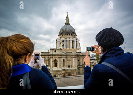 Zwei Frauen, die an einem Wintertag mit ihrem Smartphone Fotos von der St Paul’s Cathedral in London machen. Stockfoto