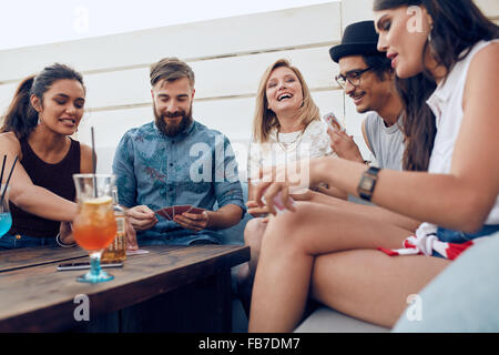 Gruppe von Freunden sitzen an einem Holztisch und Spielkarten. Fröhliche junge Menschen feiern zusammen und spielen Karten. Stockfoto