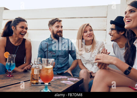 Gruppe von Freunden, die gemeinsam an einem Tisch zu entspannen. Junge Menschen hängen an einem Tisch während einer Party mit Cocktails und pla Stockfoto