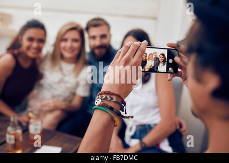 Menschen nehmen Foto seiner Freunde mit Handy. Junge Menschen sitzen zusammen auf einer Party genießen. Stockfoto