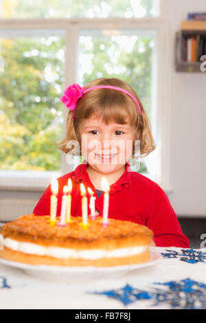 Glückliches Mädchen Blick auf Geburtstagskuchen auf Tisch Stockfoto