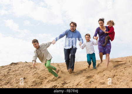 Fröhliche Familie Hand in Hand während der Ausführung auf Sanddüne gegen Himmel Stockfoto