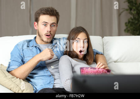 Erstaunt paar vor dem Fernseher sitzen auf einer Couch zu Hause Stockfoto