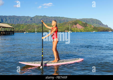 Frau auf Stand up Paddle Board in Hanalei Bay, mit Mt. Makana genannt Bali Hai und Hanalei Pier im Hintergrund Stockfoto