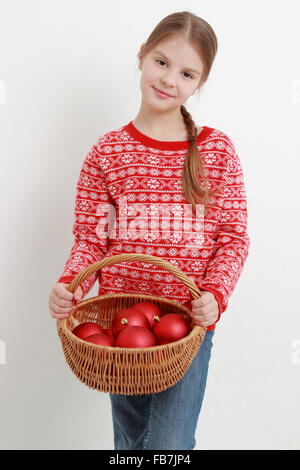 Smiley Kind trägt schöne rote Pullover und hält Weihnachtsdekoration Stockfoto