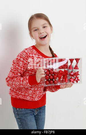 Smiley Kind trägt schöne rote Pullover und hält Weihnachtsdekoration Stockfoto