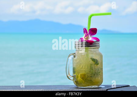 Große Gläser Becher Stil vollen Glas frisch gefrorenen Mojito mit Metallkappe Deckel, Stroh und lila Orchidee Blume im Café am Strand Stockfoto