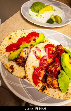 Ein Mehltortilla Chicken Taco mit Avocado, Tomate und Taco-Sauce auf einem Teller Stockfoto