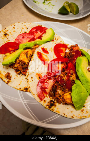 Ein Mehltortilla Chicken Taco mit Avocado, Tomate und Taco-Sauce auf einem Teller Stockfoto