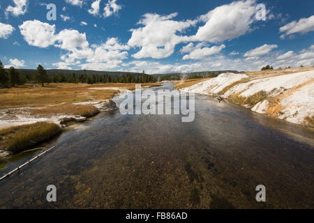 Firehole River fließt durch Kalkablagerungen des Upper Geyser Basin im Yellowstone National Park unter einem tiefblauen Himmel. Stockfoto