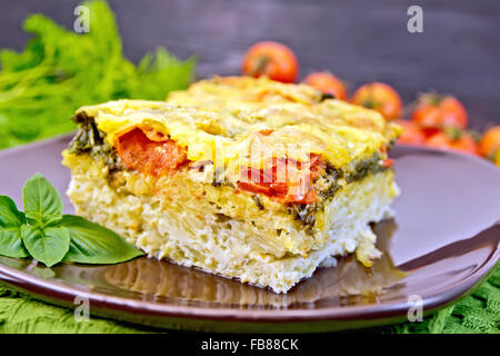 Die Torte von Kartoffeln, Käse, Tomaten und Spinat, gefüllte Ei mit Milch in einen Teller, eine Serviette gegen ein Holzbrett Stockfoto