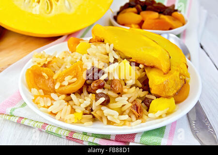 Pilaw Frucht mit Kürbis, Rosinen, getrocknete Aprikosen in einem weißen Teller auf einer Serviette, Kürbis, getrocknete Früchte, Löffel Hintergrund des Lichts Stockfoto