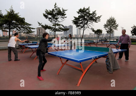 Menschen spielen in einem Park am Flussufer bei einer typischen Stadt in China Tischtennis. Stockfoto