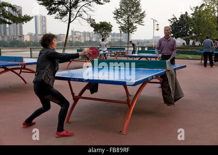 Menschen spielen in einem Park am Flussufer bei einer typischen Stadt in China Tischtennis. Stockfoto