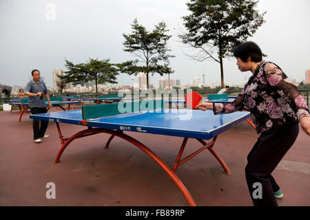 Menschen spielen in einem Park am Flussufer bei einer typischen Stadt in China Tischtennis. Stockfoto