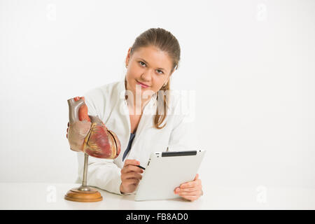 junge Ärztin arbeitet mit Modell des menschlichen Herzens und Tablet-pc Stockfoto