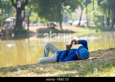 Asiatische-Generator immer Rest mit Handy in der Hand auf dem grünen Rasen in der Nähe Fluss Stockfoto