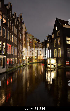 Stadthäuser und Kunstinstallation entlang der Oudezijds Achterburgwal in der Nacht, Amsterdam, Niederlande Stockfoto