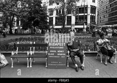 Blick auf Bupapest zum Zeitpunkt der neunziger Jahre. -1990 - Ungarn / Budapest - Blick auf Bupapest zum Zeitpunkt der neunziger Jahre. -Alltägliche Szene.  In einem öffentlichen Garten ist eine Frau stricken, während ein Mann an der Seite ein Mädchen hält eine Werbung Hinweis für eine Fremdsprachen unterrichten Schule ist.   -Philippe Gras / Le Pictorium Stockfoto