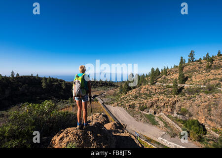 Ältere Frau Walker auf einem Felsen mit Blick auf ein Weingut auf einem Wanderweg durch eine ländliche Gegend in Guia de Isora, Teneriffa, Kanarische Stockfoto