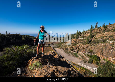 Ältere Frau Walker auf einem Felsen mit Blick auf einen Weinberg auf einem Wanderweg durch eine ländliche Gegend in Guia de Isora, Teneriffa, Stockfoto