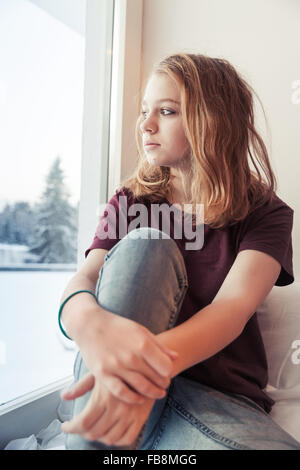 Blondes junges Mädchen sitzt in der Nähe von Winter-Fenster auf der Fensterbank und außen sieht Stockfoto