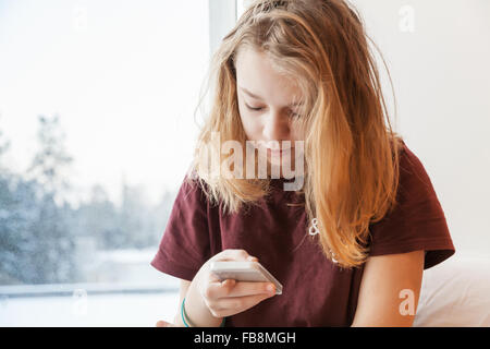 Blonde Teenager-Mädchen sitzen in der Nähe von Winter Fenster mit smartphone Stockfoto