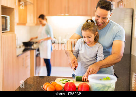 kleine Tochter Schneiden von Gemüse beim Kochen auf Hintergrund Mutter Vater Stockfoto