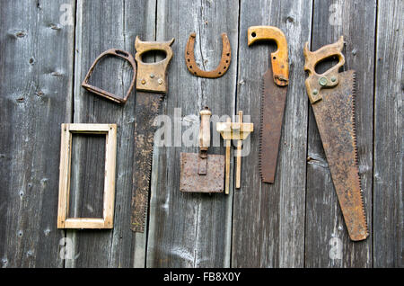Viele rostige Vintage Zimmereiwerkzeuge und Hufeisen an alten hölzernen Wand gehängt Stockfoto