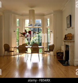 Wicker und Metall Stühle an einem einfachen Tisch mit einer Blumenvase groß in einem Stadthaus Speisesaal mit hölzernen Bodenbelag Stockfoto