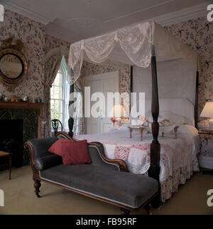 Graue Chaiselongue am Fuße des ein Himmelbett mit weißen Spitzen Vorhänge und ein Frühstückstablett Stockfoto