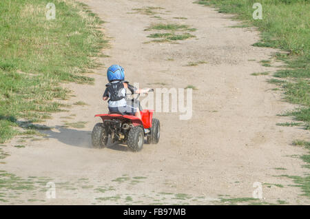 Jungen mit dem roten ATV Quad Fahrrad auf einem trockenen Feldweg an einem Sommertag Stockfoto