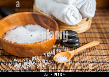 Badesalz in einer Holzschale, drei weiße Handtücher und Wellness-Steinen auf einem hölzernen Hintergrund Stockfoto