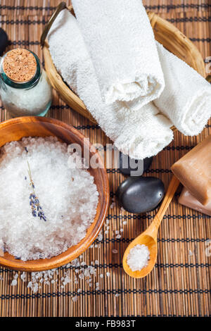 Badesalz in einer Holzschale, drei weiße Handtücher und Wellness-Steinen auf einem hölzernen Hintergrund Stockfoto