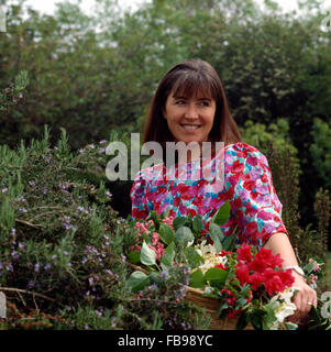 Eine lächelnde junge Frau trägt ein florales Kleid und schneiden Blumen in einem Garten in Nahaufnahme Stockfoto