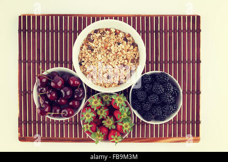 Hausgemachte Müsli und Kirschen, Erdbeeren und Brombeeren in Keramikschalen auf Bambusmatte gelegt. Bild hat Vintage-filter Stockfoto
