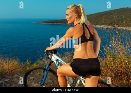 Junge Frau Radfahrer auf dem Mountainbike, Blick auf die Landschaft zwischen Bergen und Meer Stockfoto