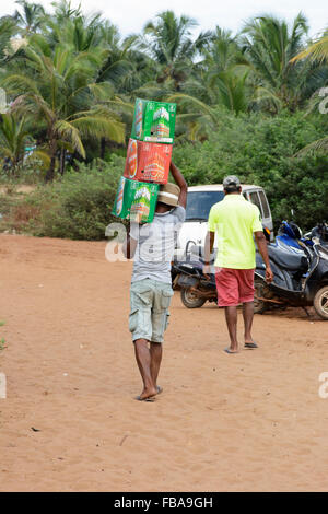 Ein indischer Junge trägt Vorräte an Bier zu einem Strandcafé am Candolim Beach in North Goa, Indien Stockfoto