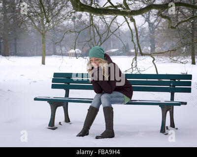 Frau sitzt alleine auf Parkbank im winter Stockfoto