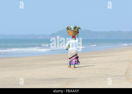 Eine indische Frau verkaufen Obst und Getränke geht entlang einer leeren Strand, Mandrem Beach, North Goa, Indien Stockfoto