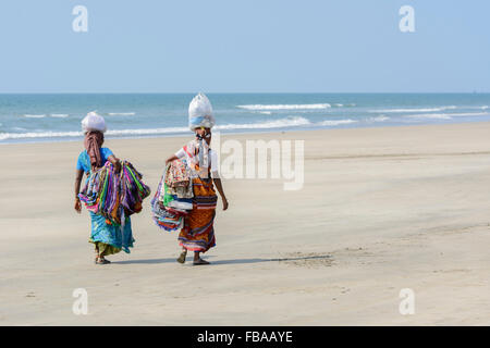 Zwei indische Frauen verkaufen Sarongs und Stoffe Spaziergang entlang eines leeren Strand, Mandrem Beach, North Goa, Indien Stockfoto