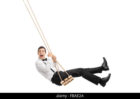 Eleganter Mann mit einer schwarzen Fliege und Strapsen schwingen auf einer Holzschaukel isoliert auf weißem Hintergrund Stockfoto